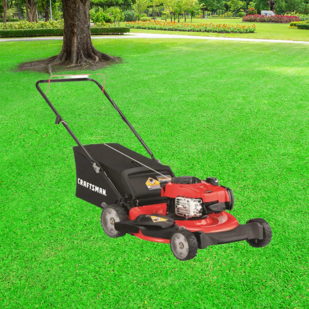 A red and black lawn mower on grass next to a tree.