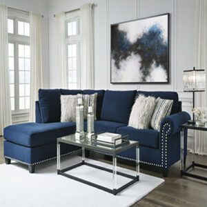 A blue sectional couch with pillows and a glass table.