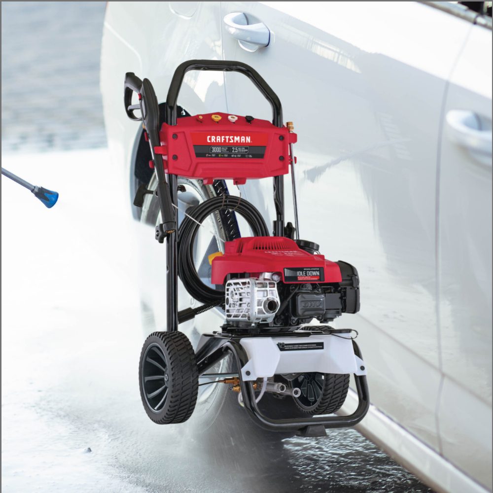 A red and black pressure washer sitting next to a white car.